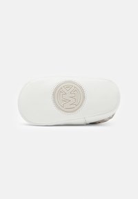 Funda de cuero blanco con una textura suave, que presenta un logotipo circular beige en el centro y un reverso con un patrón. Cierre de cremallera.
