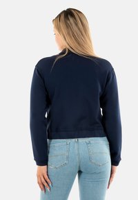 Felpa corta blu navy con maniche lunghe, polsini a coste e una superficie liscia, abbinata a jeans attillati blu chiaro.