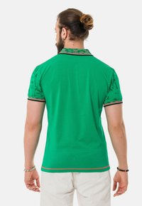 Grünes Poloshirt mit kurzen Ärmeln, ausgestattet mit einem gemusterten Kragen und kontrastierenden Akzenten. Weicher Stoff und taillierte Passform, geeignet für legere Anlässe.