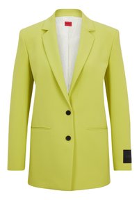 Limonkowa marynarka dopasowana, z wyraźnie zarysowanymi ramionami, dwoma czarnymi guzikami, bocznymi kieszeniami i akcentem z logo na rękawie. Gładka faktura.