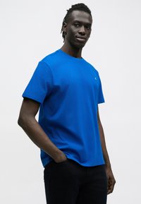 Koszulka z krótkim rękawem i okrągłym dekoltem w żywym niebieskim kolorze, wykonana z bawełny, z subtelnym logo na lewej piersi, zestawiona z ciemnymi dżinsami.