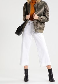 Sametová olivově zelená bomber bunda, rezavý rolák, bílé zkrácené široké kalhoty, černé kotníkové boty a černá crossbody taška.