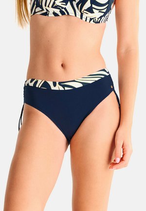 Femme portant un bas de bikini bleu marine avec une large ceinture à motifs et des liens latéraux assortis au haut du bikini, vue du nombril aux cuisses.