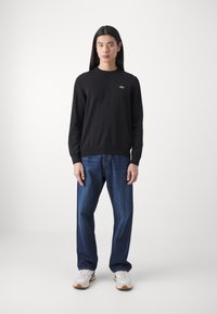 Sort sweater med lange ærmer, ribbet kant og subtilt logo. Sammen med blå lige bukser og hvide sneakers.