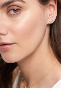 Goldohrringe mit dem Wort "LIEBE", verziert mit kleinen klaren Edelsteinen, die eine zarte Goldkettenschnur ergänzen.