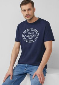 Navyblauwe katoenen t-shirt met een witte cirkelvormige graphic en tekstdetails. Korte mouwen, ronde hals en een relaxed fit.