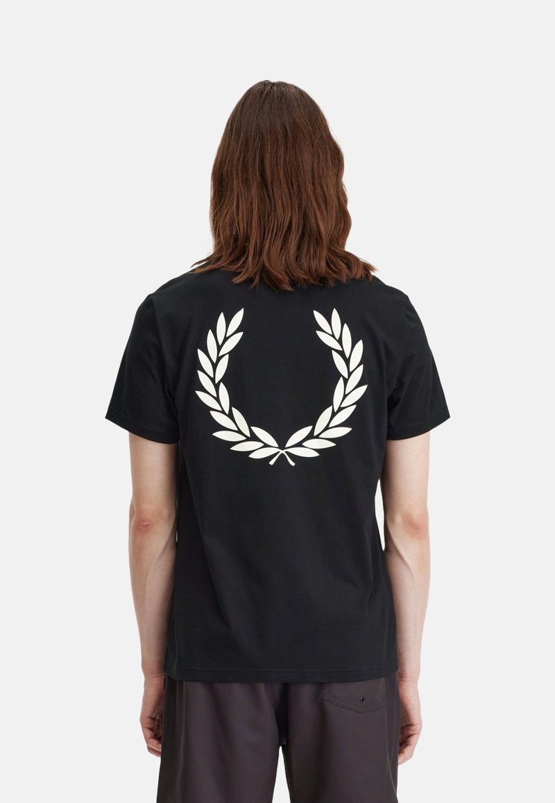 Camiseta corta negra de algodón con un gran gráfico blanco de una corona de laurel en la parte de atrás. Cuello redondo sencillo y corte relajado.