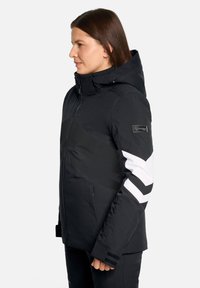 Schwarze Winterjacke mit Kapuze, mit weißen diagonalen Streifen, Reißverschlusstaschen und einer strukturierten Oberfläche. Mit Branding auf dem Ärmel.