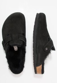 Zoccoli in suede nero con fodera in pelliccia, cinturini regolabili e soletta in sughero. Suola in gomma textured per una migliore aderenza e durata.