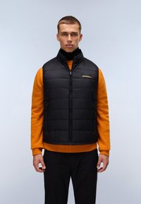 Sort polstret vest med høj krave, lynlås foran og sidelommer, båret over en orange sweater. Glat tekstur med kontrasterende farver.