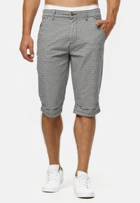 Schwarz-weiße karierten Bermuda-Shorts aus leichtem Stoff, mit Knopfverschluss und umgeschlagenen Säumen. Getragen mit weißen Sneakers.