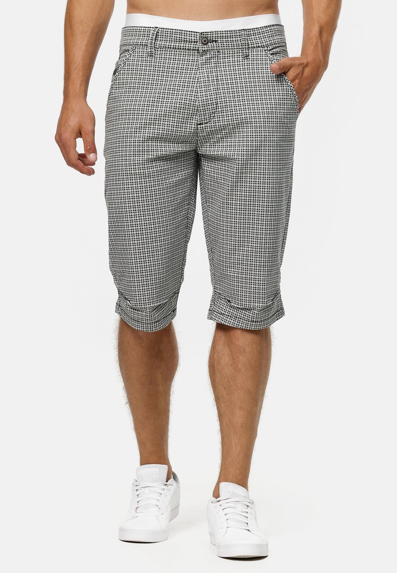 Checked black and white bermuda shorts made of lightweight fabric, featuring a button closure and rolled cuffs. Worn with white sneakers.