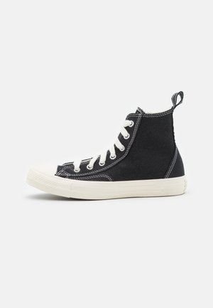 Baskets montantes noires en toile avec des lacets blancs et des semelles en caoutchouc. Elles présentent des détails de coutures et un languette de traction au talon.