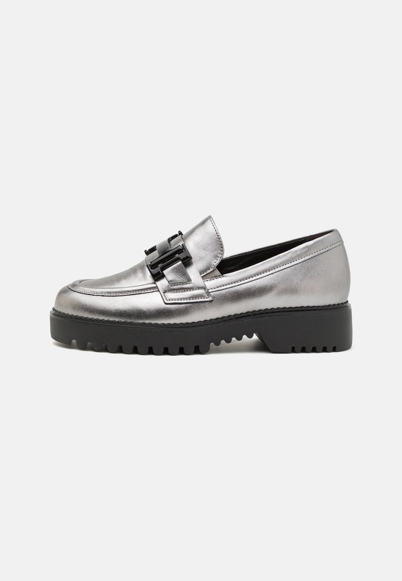Mocassins argent métalliques avec une semelle noire épaisse, dotées d'une boucle décorative sur le dessus. Texture lisse et design à bout arrondi.