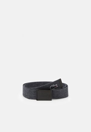 Ceinture en tissu gris foncé enroulée avec une boucle rectangulaire noire embossée de "Lacoste" et petit logo de crocodile brodé à l'extrémité de la lanière.