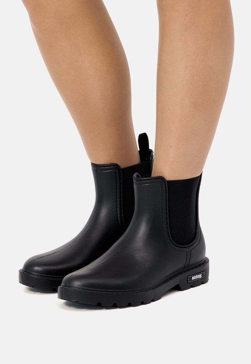 Botas de tobillo de goma negra con paneles laterales elásticos y suelas texturizadas. Acabado liso con una pestaña para facilitar su colocación.