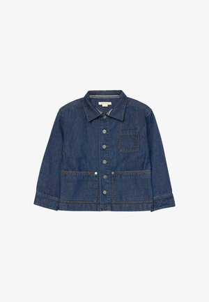 Barn iført en blå denimjakke med metal-knapper og flere frontlommer, kiggende nedad mod en ensfarvet baggrund.