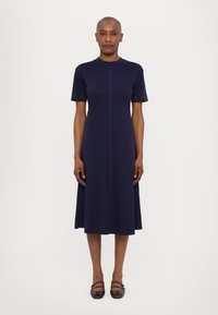 Marineblaues Midikleid mit kurzen Ärmeln, einem runden Ausschnitt und einer zentralen Naht. Hergestellt aus einem glatten Stoff, der dezente kontrastierende Nähte aufweist.