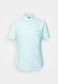 Světle modrá košile s krátkým rukávem vyrobená z bavlny. Obsahuje límec na knoflíky a malé vyšívané logo na hrudi.