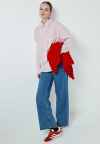 Camicia a righe bianca e rossa, jeans a gamba larga blu, maglione rosso a maglia appoggiato, e scarpe da ginnastica retro rosse e bianche.