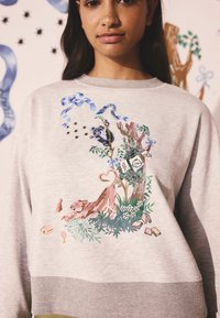 Hall hallipluus, millel on lühendatud disain ja värvikas loomade ning taimede tikand. Silmapaistvad detailid hõlmavad siniseid paelu ja lillelisi aksente.