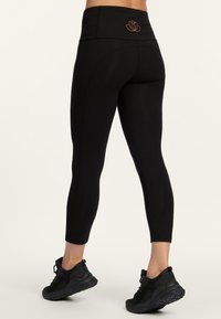 Zwarte high-waisted legging gemaakt van rekbaar materiaal, met een lotusontwerp in oranje op de achterkant en een aansluitende, korte pasvorm.