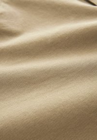 Beżowa tkanina teksturowana z subtelnym wzorem tkanym, pokazująca miękki, trwały materiał odpowiedni do różnych zastosowań.