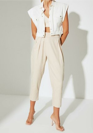 Witte cropped denimjas met korte mouwen, gecombineerd met beige geplooide broeken en doorzichtige sandalen met hoge hakken. Gladde texturen en neutrale kleuren.