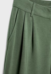 Krupni plan maslinasto zelenih hlača koje prikazuju nabore, bočni džep, pojas i petlju za remen.