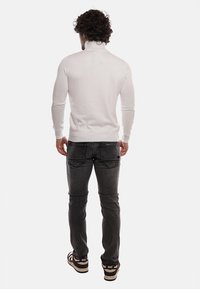 Pullover bianco a maniche lunghe con colletto alto, abbinato a jeans grigio scuro e sneaker nere con dettagli bianchi. Tessuto morbido, stile aderente.