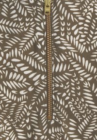 Gros plan d'une fermeture éclair dorée sur un tissu avec un motif abstrait de feuilles marron et blanc.