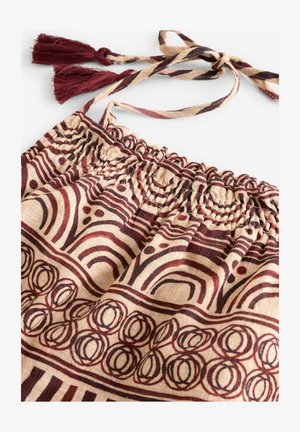 Textiel tas met een geplooide top, voorzien van een bruine en crème patronen ontwerp, afgewerkt met franjes aan verstelbare banden.