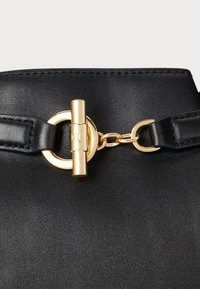 Juodas odinis rankinės su aukso atspalvio aksesuaru, grandine ir užsegimu, demonstruoja glotnų ir tekstūruotą paviršių.