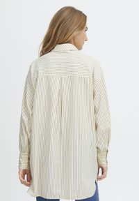 Striped long-sleeve shirt in cream and light brown, featuring a buttoned cuff, different fabric textures, and a relaxed fit design.