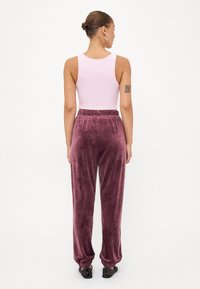 Paarse fluwelen joggingsbroek met een elastische tailleband en enkelmanchetten, gecombineerd met een lichtroze mouwloos topje. Gladde textuur overal.