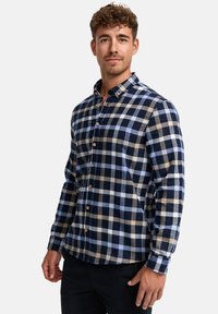 Camisa de cuadros abotonada en navy, azul claro y marrón. Confeccionada con tela suave, cuenta con un collar clásico y botones de madera. Ajuste entallado.