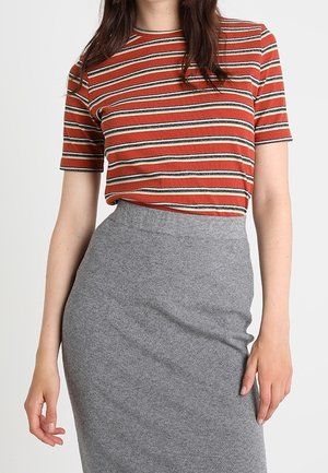 Femme portant un haut à rayures orange rouille, noir et blanc à manches courtes, rentré dans une jupe grise ajustée à taille haute.