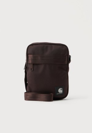 Malá tmavohnedá Carhartt taška na rameno s predným vreckom na zips a nastaviteľným popruhom na bielom pozadí.