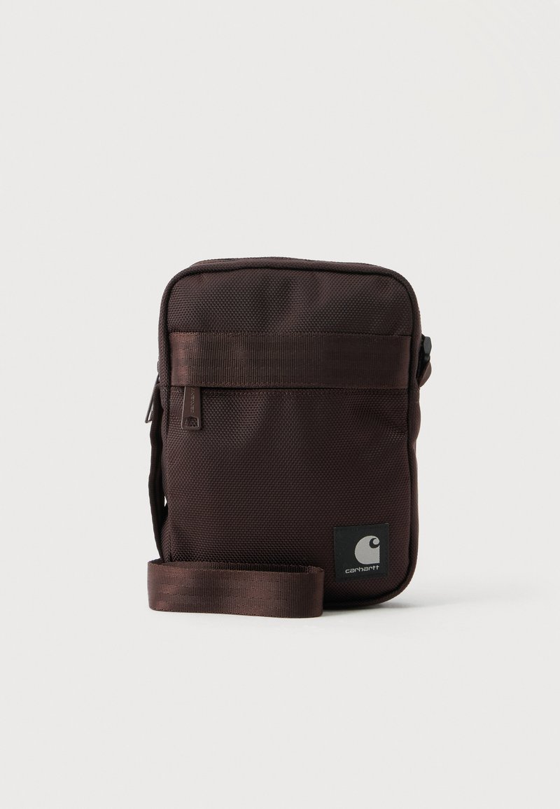Μικρή σκούρα καφέ τσάντα ώμου Carhartt με μπροστινή τσέπη με φερμουάρ και ρυθμιζόμενο ιμάντα σε λευκό φόντο.