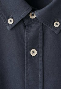 Camicia button-up blu navy con colletto classico, bottoni bianchi con cuciture nere e tessuto testurizzato con un sottile motivo a trama.