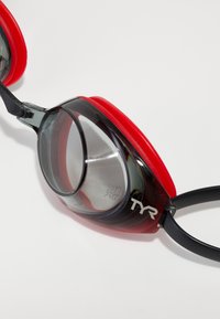 Swimming goggles with a grey-black frame, red silicone seals, and clear lenses featuring the TYR logo on the side.