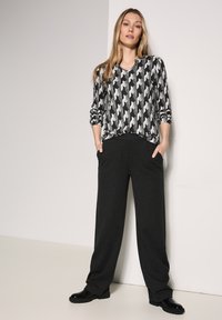 Pitkähihaiset paita musta-harmaassa houndstooth-kuviossa, V-pääkappaleella, yhdistettynä löyhästi istuviin mustiin housuihin ja mustiin chunky-kengiin.
