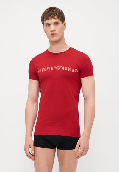 T-shirt rouge en coton à manches courtes présentant le logo "Emporio Armani" dans des couleurs contrastantes. Design ajusté, encolure ronde simple, texture lisse.