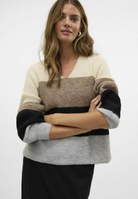 Pulover s V-izrezom v barvah krema, bež, črne in sive; rebrasta tekstura; ohlapen kroj z oversized rokavi; mehak pleteni material.