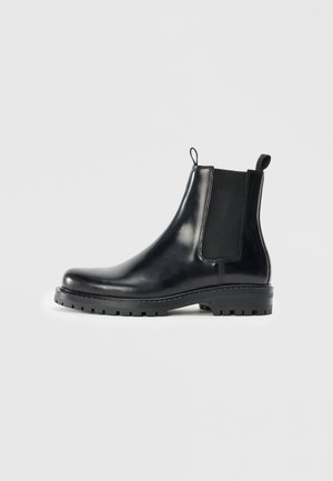 Botas Chelsea de cuero negro con paneles laterales elásticos, una pestaña de bucle para facilitar el uso y una suela de goma resistente con un agarre texturizado.