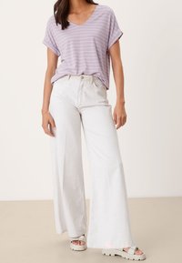Camiseta de rayas moradas claras con escote en V y mangas enrolladas, combinada con pantalones anchos blancos y sandalias de plataforma blancas.