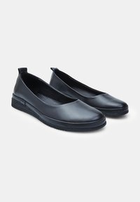 Bailarinas de cuero negro con punta redondeada, textura suave y suela de goma baja. Pequeña pestaña en el talón para facilitar el calzado.