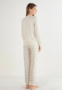 Lichtbeige pyjamapakket bestaat uit een lang mouwtop en een patroonbroek met kleine zwarte hartjes, gemaakt van zacht katoenmateriaal.