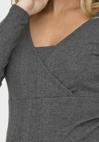 Grau langärmliges Oberteil aus geripptem Stoff mit V-Ausschnitt. Besitzt eine schichtartige Optik mit taillierter Passform und subtiler Textur.