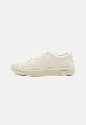 Baltas ādas sporta kurpes ar teksturētu apdari, apaļu purngalu, platiem šņorēm un biezu, bēšu gumijas zoli, kurai ir logotipa elements uz papēža.